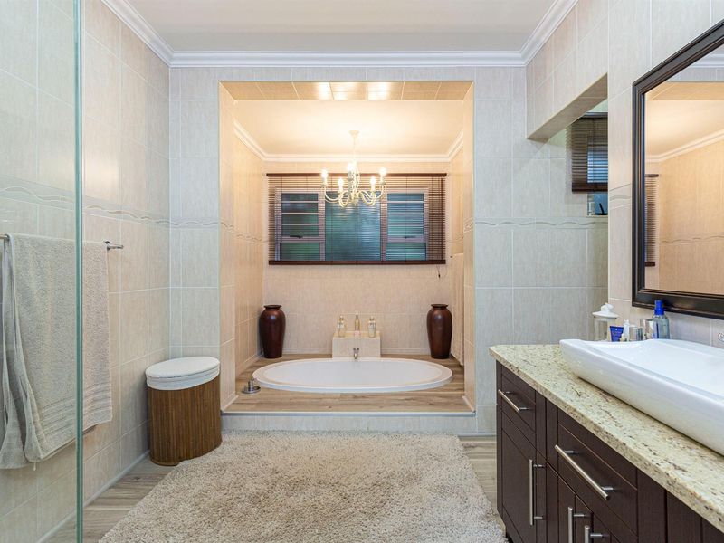 A well-appointed bathroom featuring a sunken bathtub, a modern vessel sink on a granite vanity, and a glass-enclosed shower with neutral wall tiling.