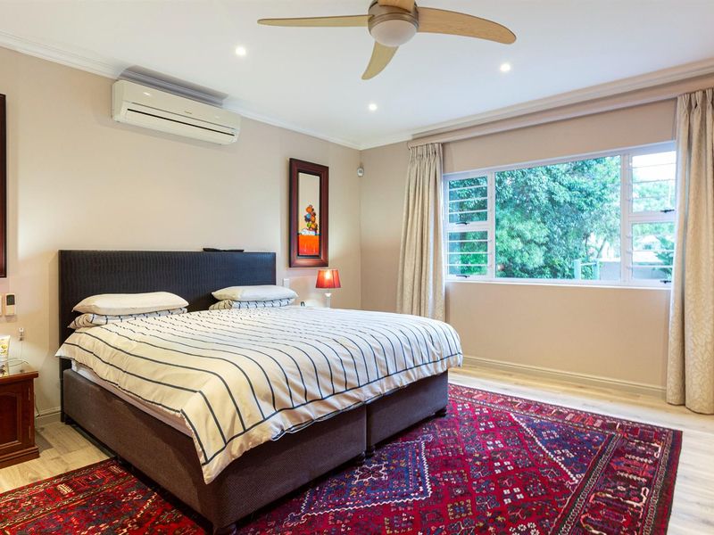 A well-maintained bedroom featuring laminate flooring, recessed lighting, a ceiling fan, and a wall-mounted air conditioning unit with a view of the garden.
