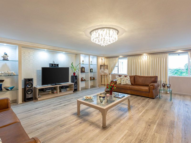 Spacious living room featuring modern laminate flooring, built-in display shelving with integrated lighting, and an elegant crystal chandelier.