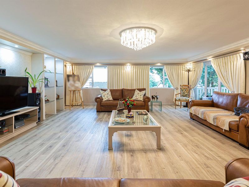 Spacious living room featuring light wood-look laminate flooring, built-in display shelving, elegant crown molding, and a central crystal chandelier.