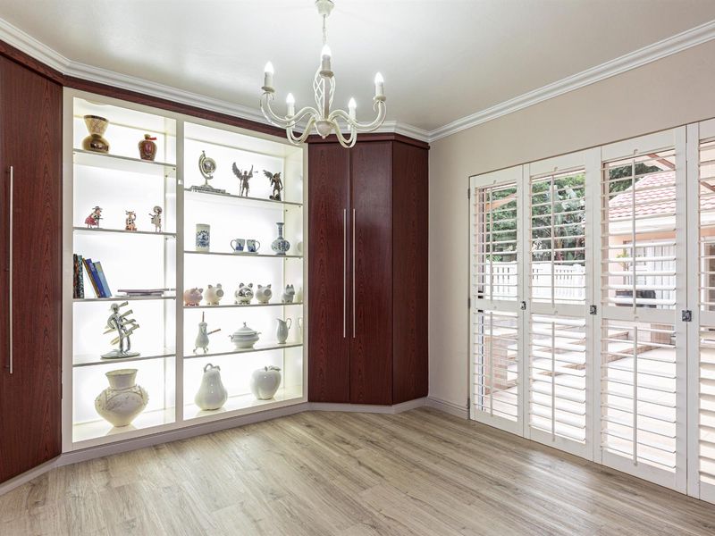 A well-maintained living area featuring custom built-in cabinetry with integrated display lighting, wood-look laminate flooring, and plantation shutters opening to the exterior.