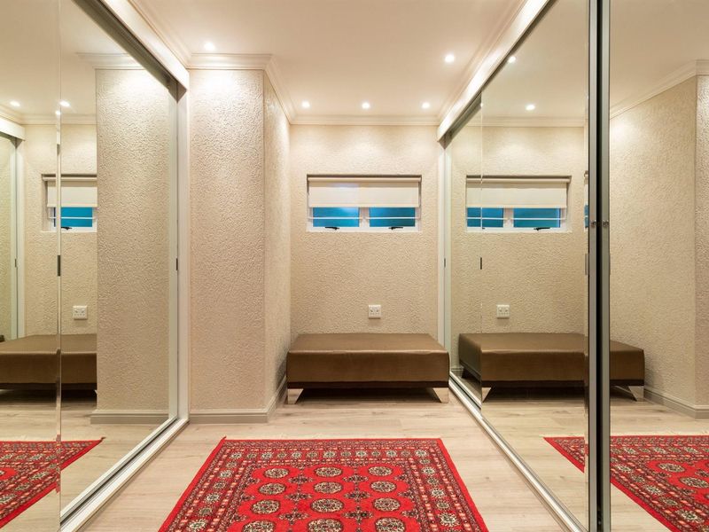 A well-maintained dressing area or bedroom featuring extensive floor-to-ceiling mirrored sliding wardrobes, recessed lighting, and modern laminate flooring.