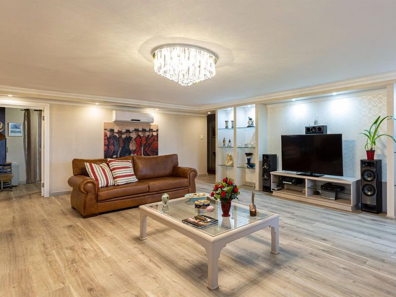 Spacious living room featuring modern laminate flooring, built-in display shelving with integrated lighting, and a decorative crystal chandelier.