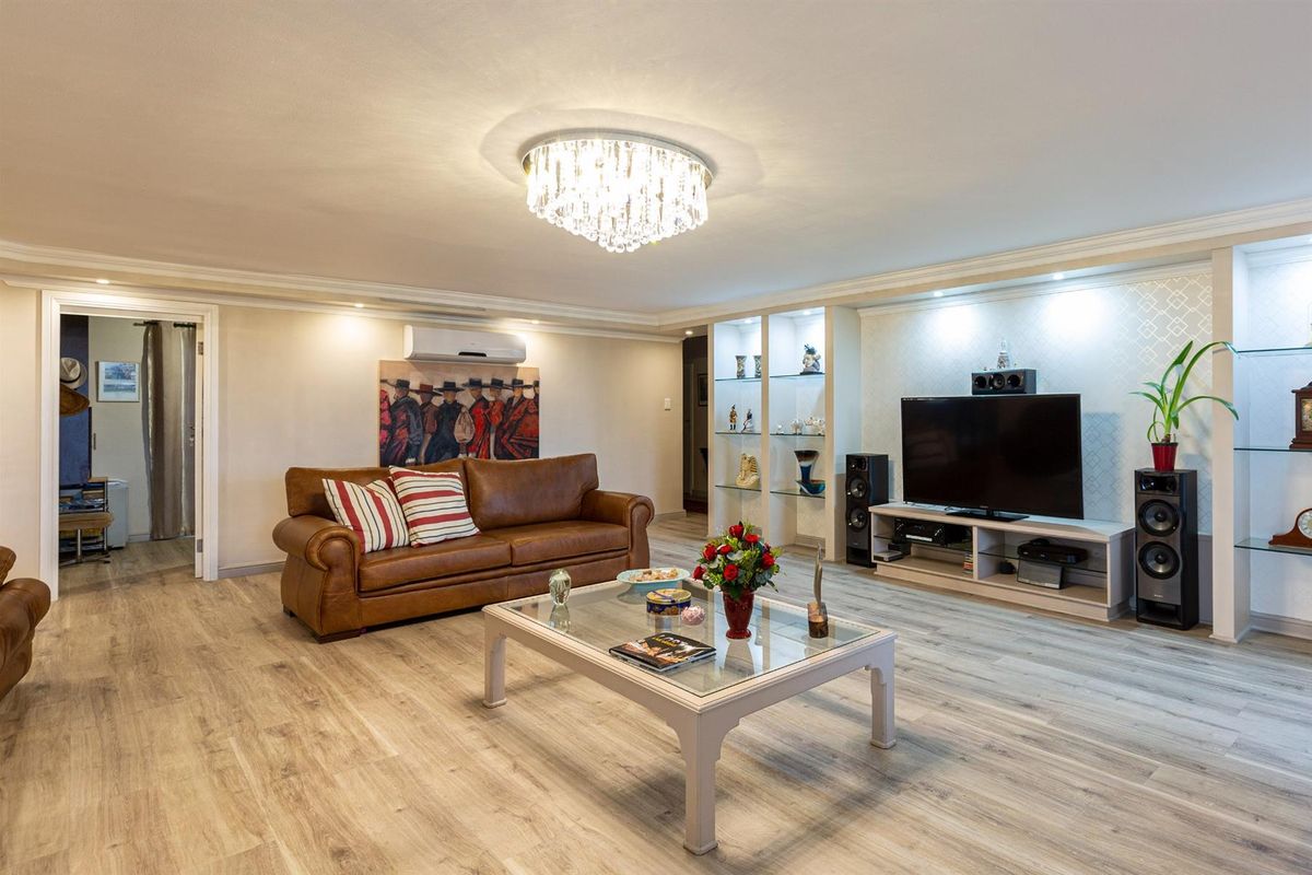 Spacious living room featuring modern laminate flooring, built-in display shelving with integrated lighting, and a decorative crystal chandelier.