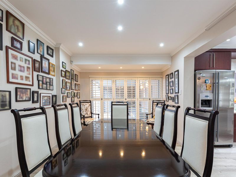 A well-lit dining room featuring crown molding, plantation shutters, and laminate flooring, with an open-plan transition to the adjacent kitchen area.