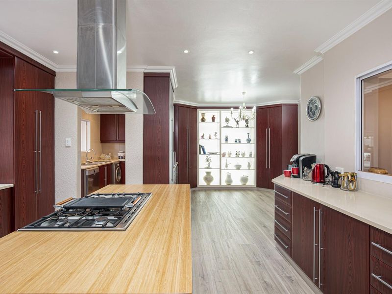 Spacious kitchen featuring a large island with a gas cooktop, stainless steel extractor, ample dark wood cabinetry, and a built-in illuminated display cabinet.