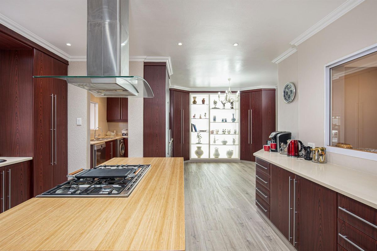 Spacious kitchen featuring a large island with a gas cooktop, stainless steel extractor, ample dark wood cabinetry, and a built-in illuminated display cabinet.
