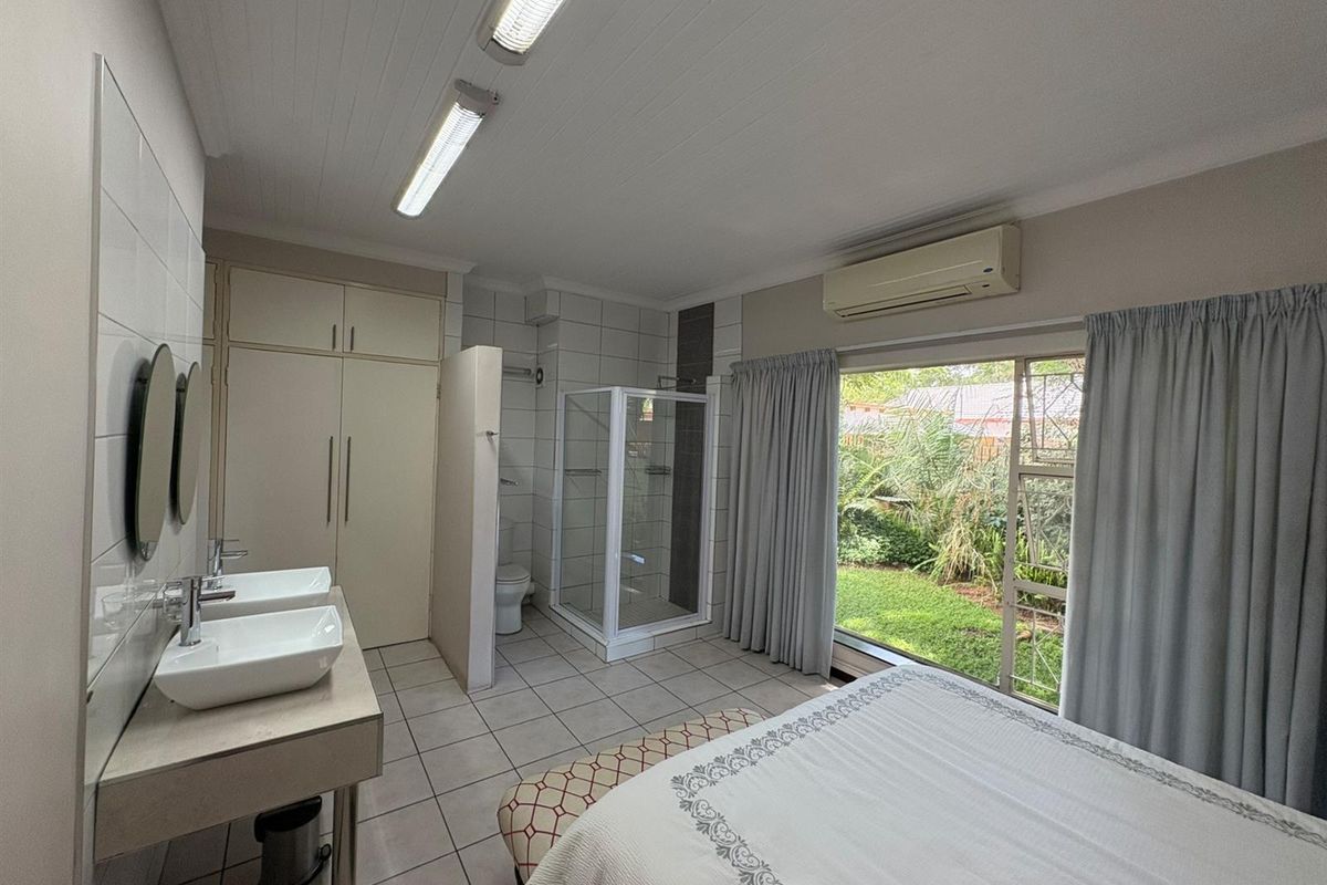 Spacious bedroom featuring an integrated en-suite bathroom with dual vanity, glass shower enclosure, and direct access to the garden through large sliding doors.