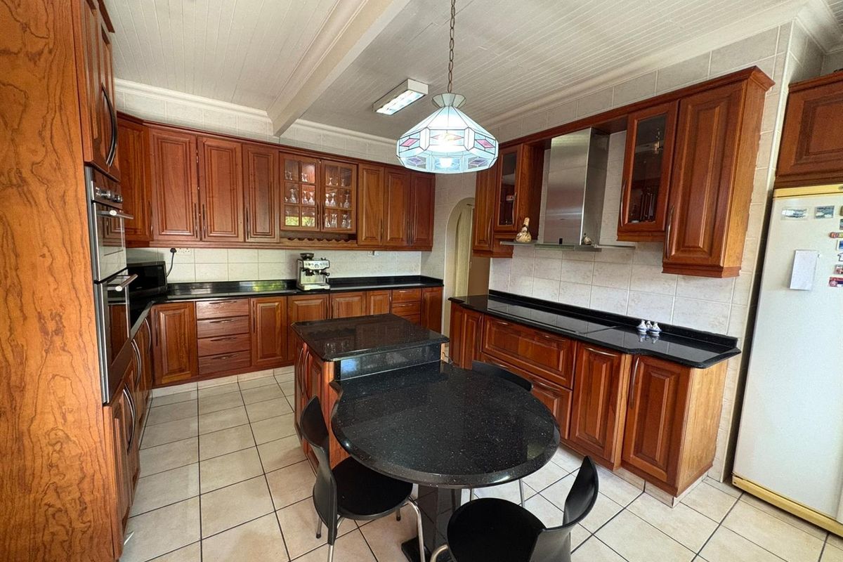 A spacious kitchen featuring traditional timber cabinetry, black granite countertops, tiled flooring, and a central island with integrated dining space.
