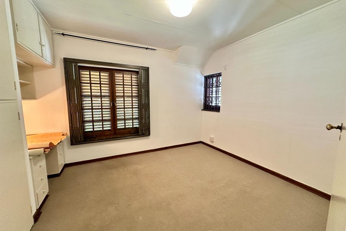 A functional bedroom featuring built-in cabinetry, carpeted flooring, and security shutters on the windows.