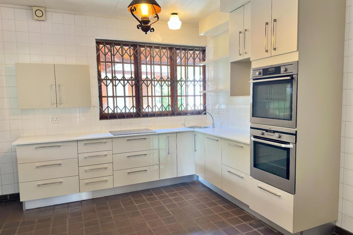 A functional kitchen featuring white cabinetry, built-in double ovens, a cooktop, and a window with security bars.