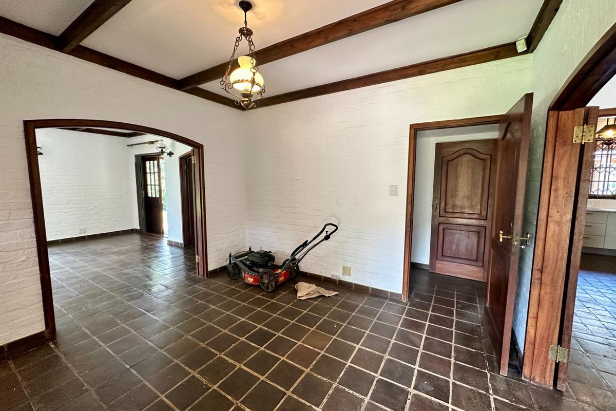 An interior living space featuring exposed timber ceiling beams, white painted brick walls, and dark ceramic floor tiles with an arched entryway.