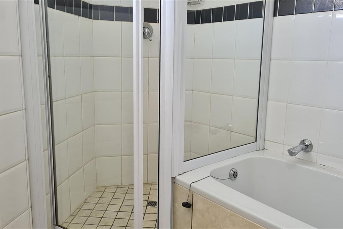 A functional bathroom featuring a combined shower and bathtub unit with white wall tiling and a contrasting dark border.