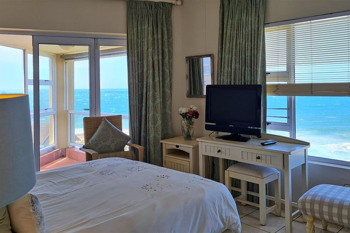 A bright bedroom featuring large windows and sliding glass doors that provide expansive ocean views and access to a private balcony.