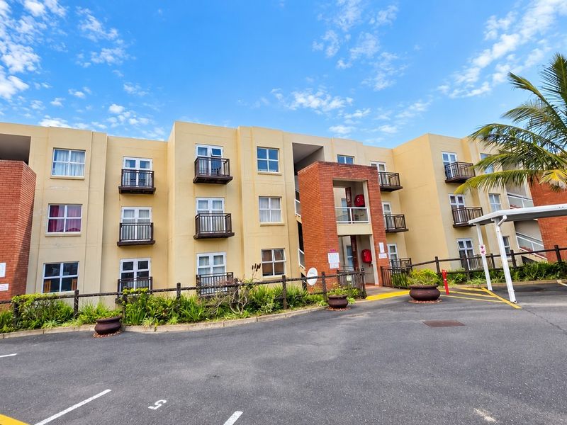 Exterior view of a multi-story apartment complex featuring brick accents, private balconies, and an adjacent paved parking area with covered bays.