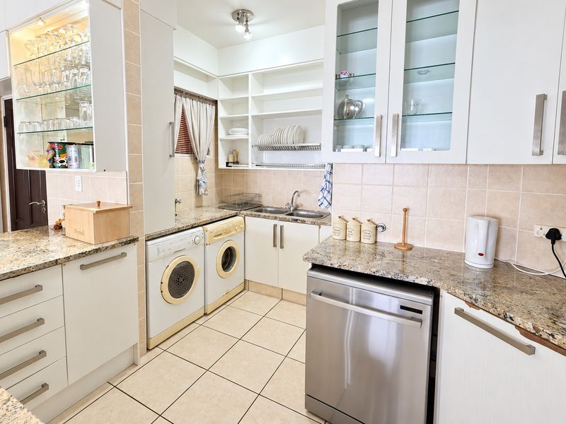A functional kitchen featuring granite countertops, ample built-in cabinetry, glass-front display units, and dedicated spaces for laundry appliances and a dishwasher.