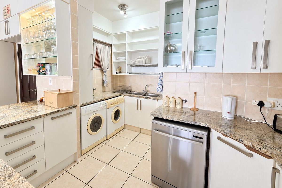 A functional kitchen featuring granite countertops, ample built-in cabinetry, glass-front display units, and dedicated spaces for laundry appliances and a dishwasher.
