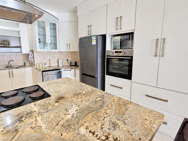 Modern kitchen featuring granite countertops, built-in cabinetry, integrated oven, electric hob, and a stainless steel sink with a tiled backsplash.