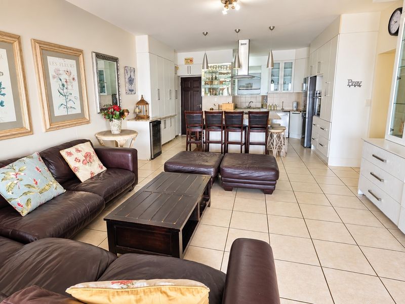 Spacious open-plan living and kitchen area featuring tiled flooring, modern cabinetry, a central kitchen island, and integrated appliances.