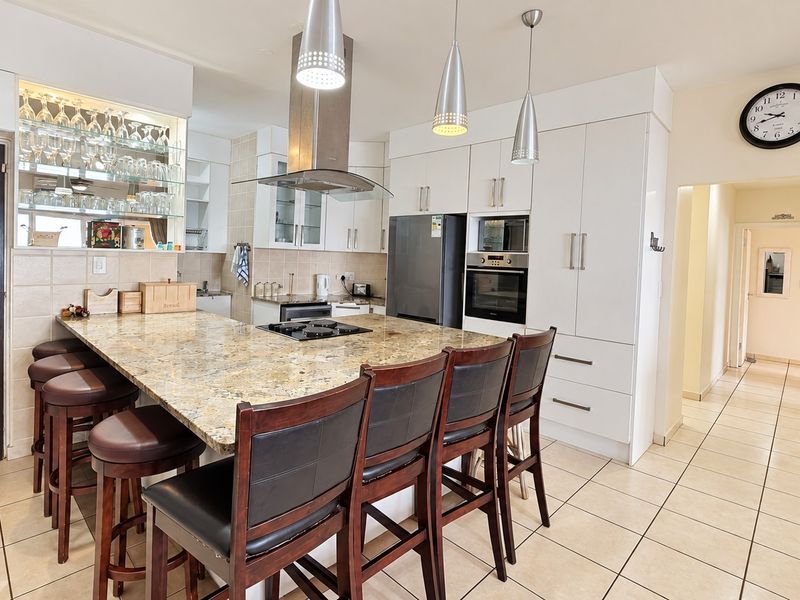Modern kitchen featuring granite countertops, built-in oven and microwave, stainless steel extractor fan, and ample cabinetry with integrated glass display shelving.