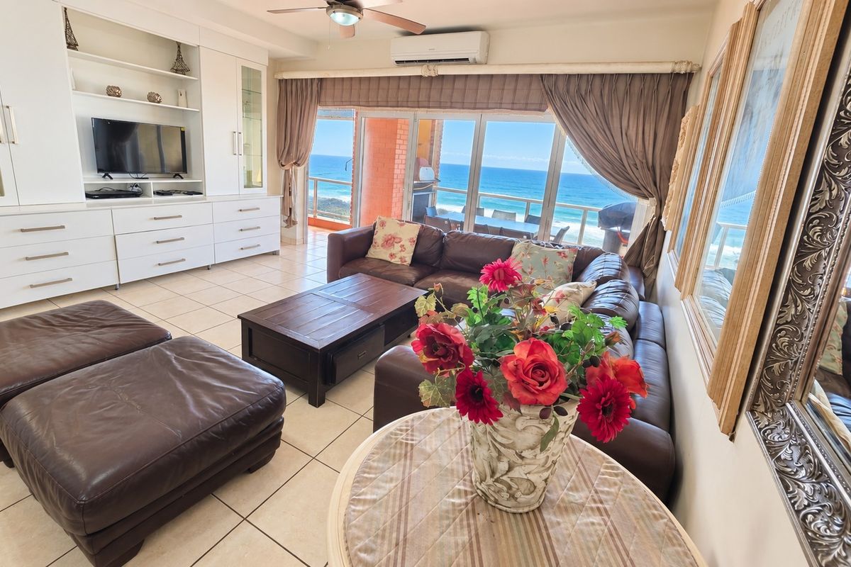 Spacious living room featuring built-in cabinetry, tiled flooring, and large sliding glass doors opening to a balcony with expansive ocean views.