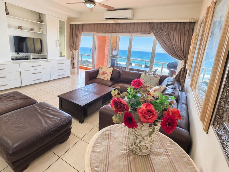 Spacious living room featuring built-in cabinetry, tiled flooring, and large sliding glass doors opening to a balcony with expansive ocean views.