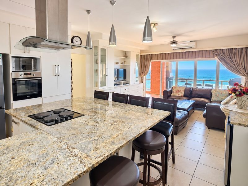 Spacious open-plan kitchen and living area featuring granite countertops, built-in appliances, and direct access to a balcony with ocean views.