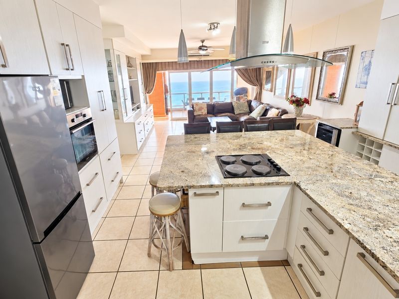 Spacious open-plan kitchen and living area featuring a large granite island, modern built-in appliances, and direct access to a balcony with ocean views.