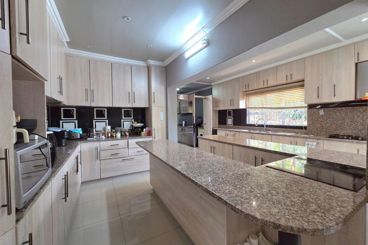 Spacious kitchen featuring light wood cabinetry, granite countertops, a large central island with a built-in cooktop, and tiled flooring.