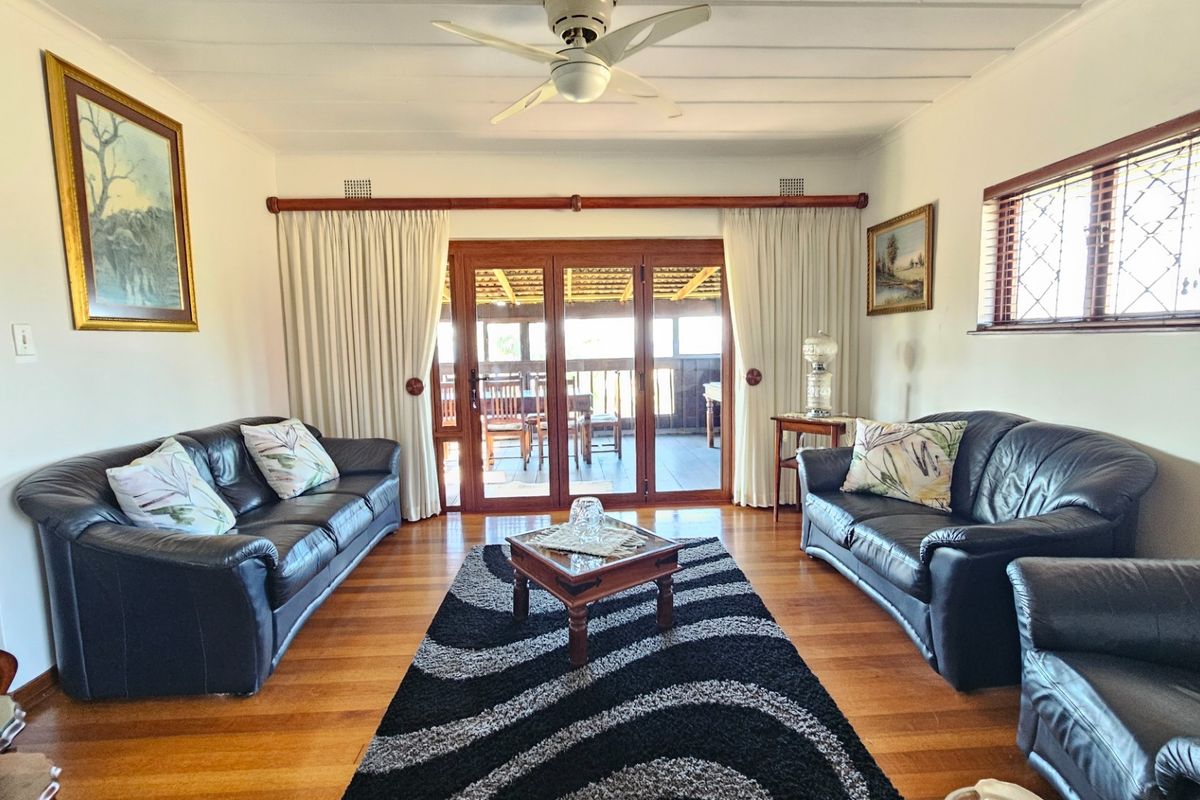 A comfortable living room featuring polished hardwood flooring, a ceiling fan, and timber-framed sliding doors providing access to an outdoor patio area.