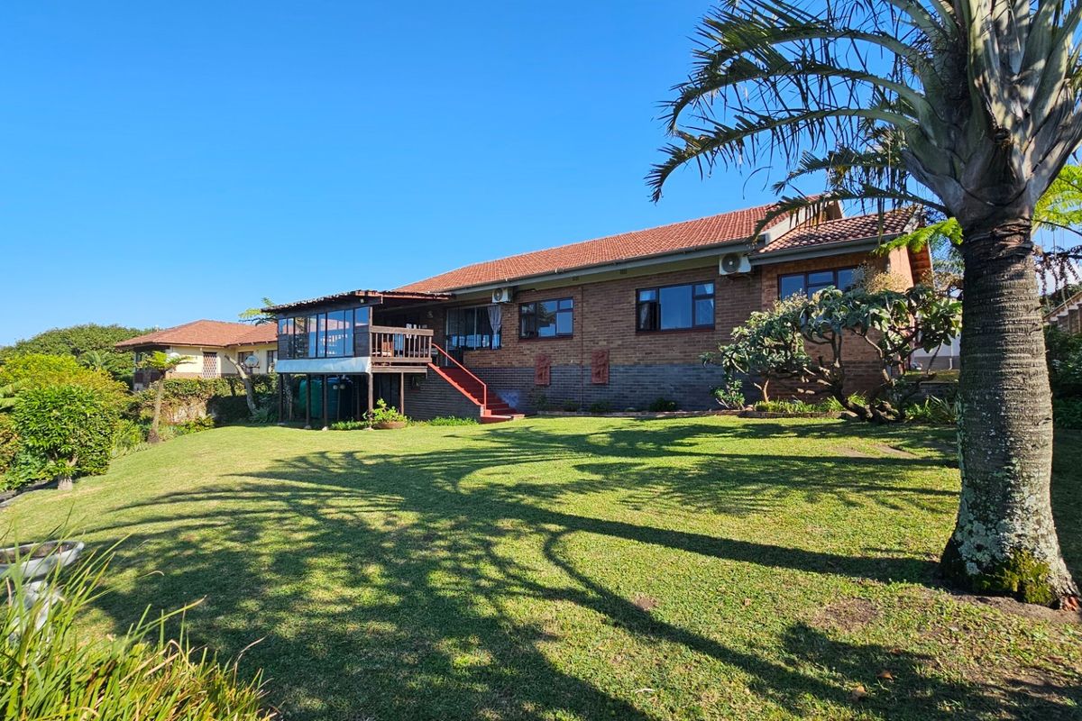 Rear view of a brick house featuring a raised timber deck, staircase, and a spacious landscaped garden.