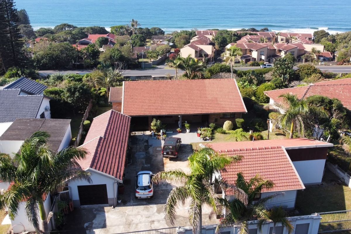 Aerial view of the property showing the main dwelling, garage, driveway, and surrounding coastal neighborhood landscape.