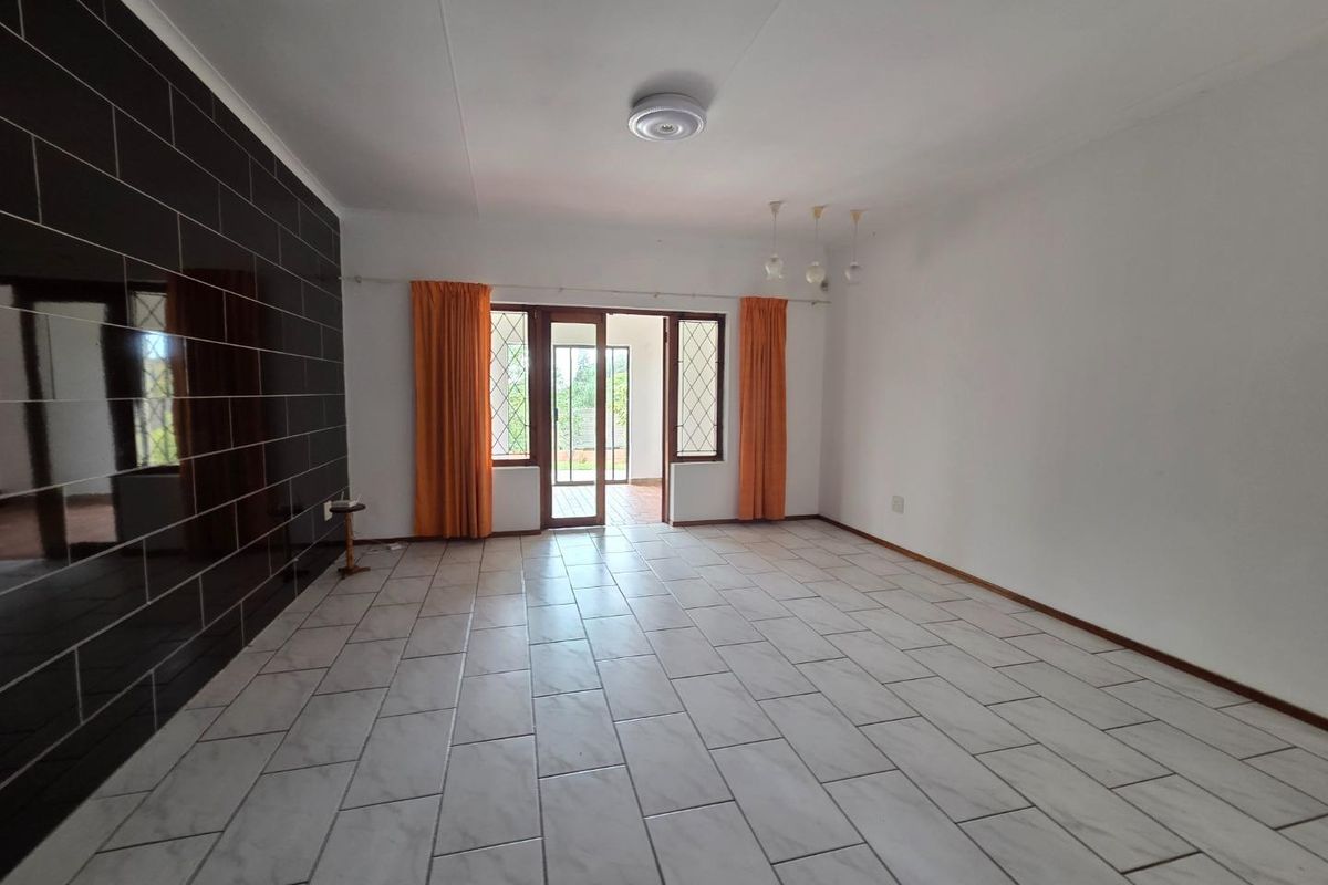 Spacious, empty living area featuring large format floor tiles, a dark tiled feature wall, and direct access to an outdoor patio area.