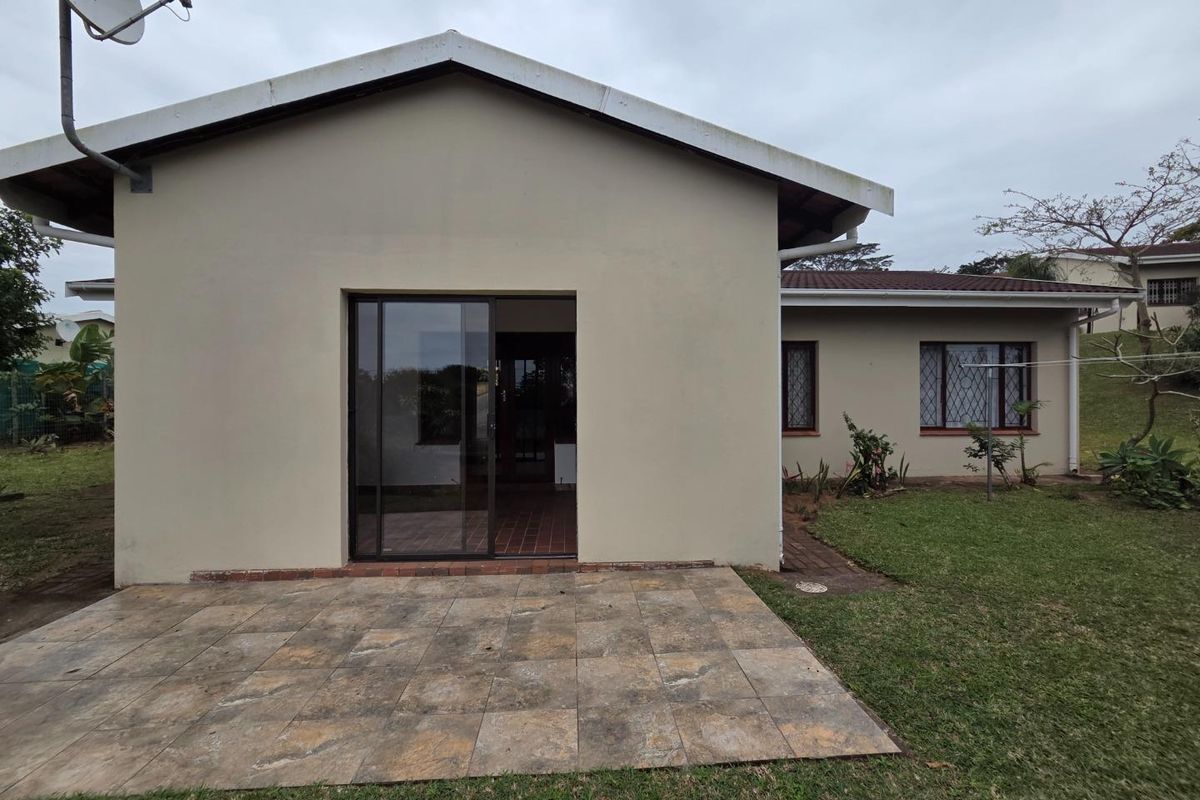 Rear view of the townhouse featuring a paved patio area, sliding glass door access, and a surrounding garden space.