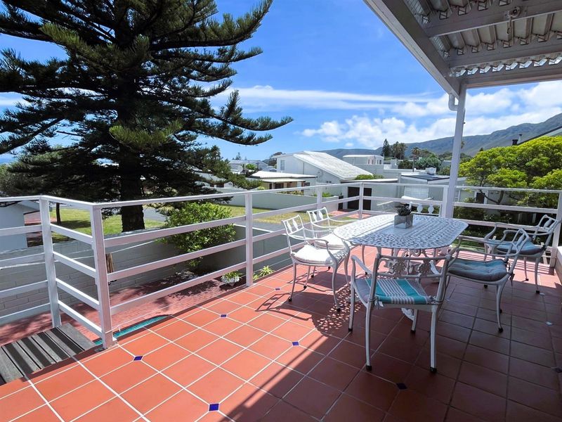 A spacious elevated balcony featuring tiled flooring, a protective metal railing, and a covered roof structure with scenic neighbourhood and mountain views.