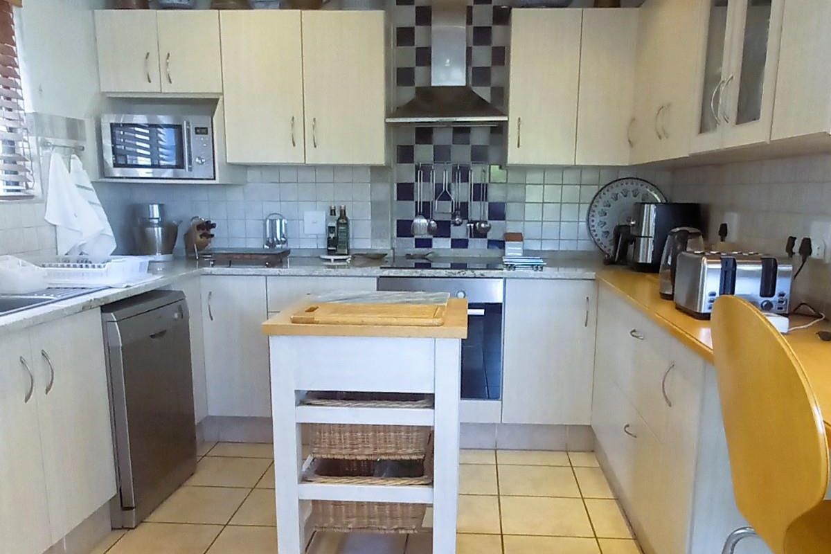A functional kitchen featuring light-toned cabinetry, a tiled splashback, built-in oven with extractor fan, and tiled flooring throughout.