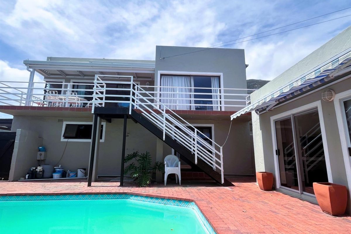 Rear exterior view featuring a swimming pool, brick paved patio, and an external staircase leading to an upper-level balcony with sliding door access.