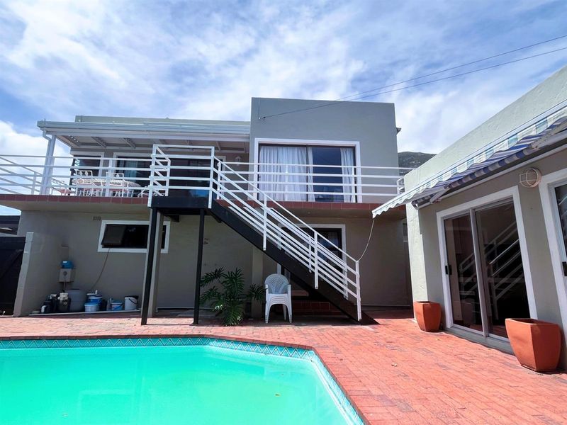 Rear exterior view featuring a swimming pool, brick paved patio, and an external staircase leading to an upper-level balcony with sliding door access.