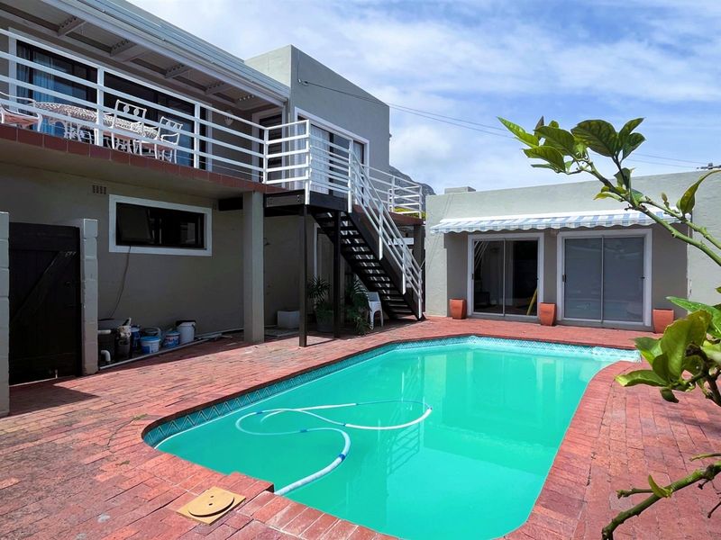 Outdoor pool area featuring brick paving, a swimming pool, an external staircase leading to an upper balcony, and sliding door access to the home.