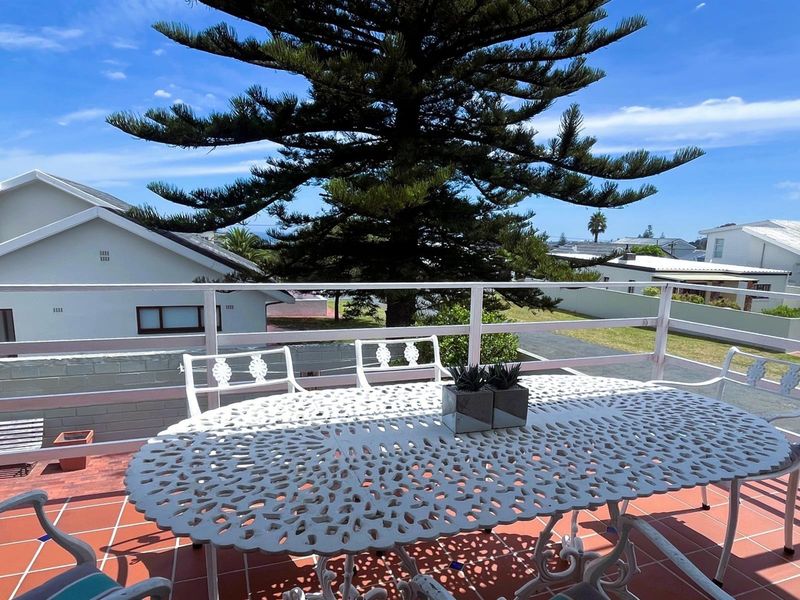 An elevated outdoor balcony featuring tiled flooring and a metal balustrade, offering an open view of the surrounding neighborhood and mature trees.