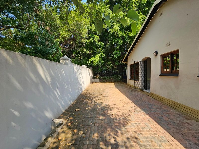 A paved side courtyard area featuring a high boundary wall, mature trees, and direct access to the home through a security gate.