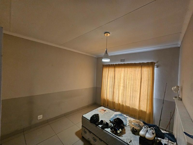 A simple bedroom featuring tiled flooring, neutral wall tones, and a window fitted with curtains.