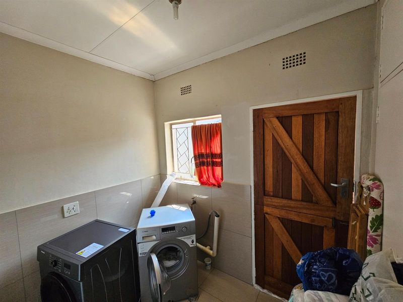 Functional laundry room featuring tiled splashbacks, plumbing connections for appliances, and a solid timber door with external access.