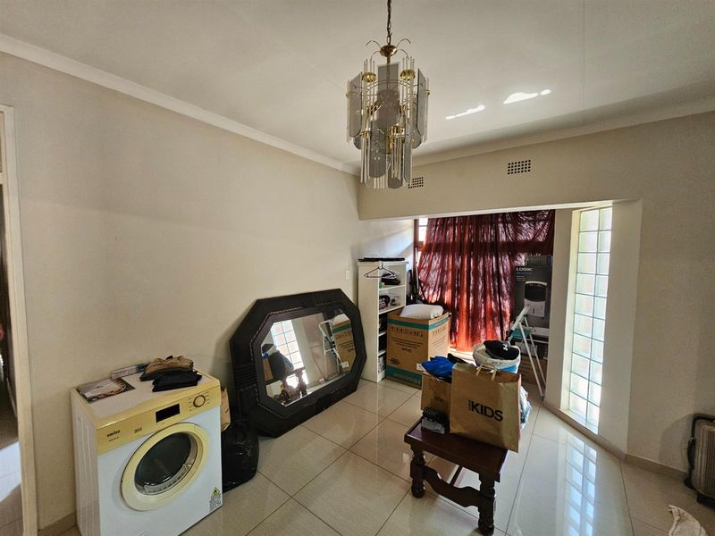 A multi-purpose room featuring tiled flooring, a decorative chandelier, and a glass block window feature, currently utilized as a utility and storage space.