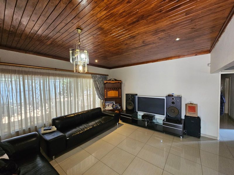 Spacious living room featuring polished tile flooring and a distinctive timber-paneled ceiling with a central chandelier.