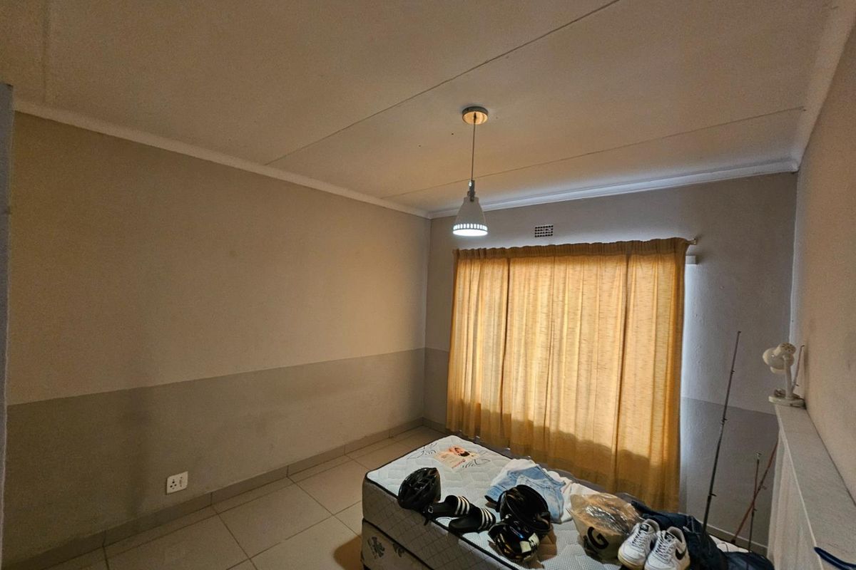A simple bedroom featuring tiled flooring, neutral wall tones, and a window fitted with curtains.