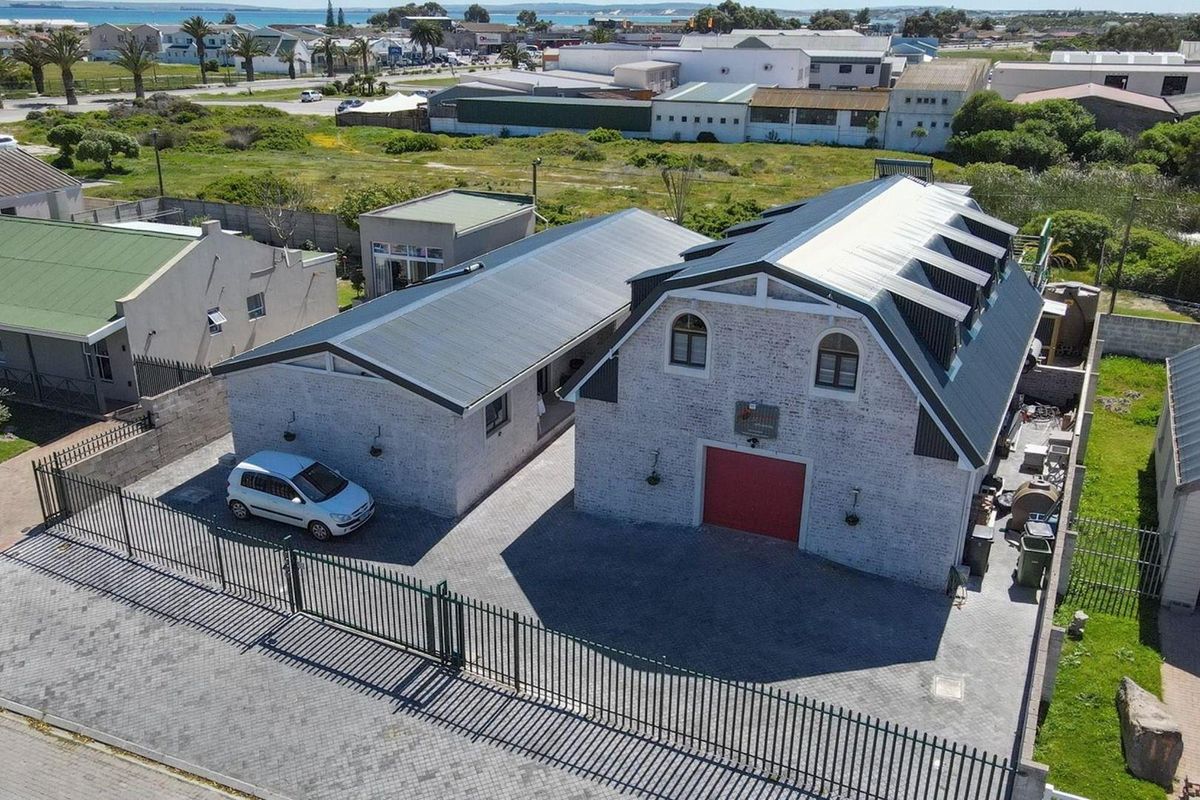 Aerial view of the property featuring a multi-building layout with metal roofing, brick exterior, paved driveway, and secure perimeter fencing.