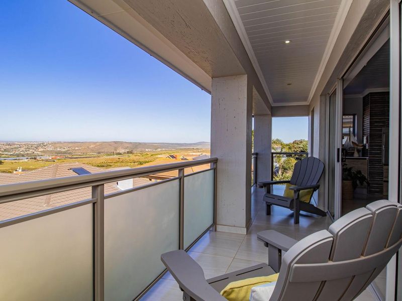 A spacious covered balcony featuring tiled flooring, modern glass and metal balustrades, and expansive panoramic views of the surrounding landscape.
