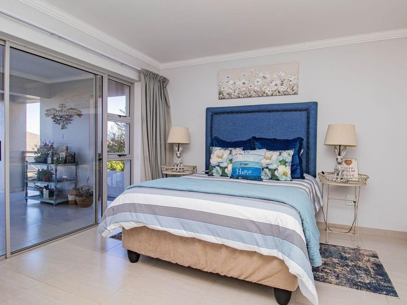 A bright bedroom featuring built-in cupboards, tiled flooring, and large sliding glass doors that open onto a private balcony.
