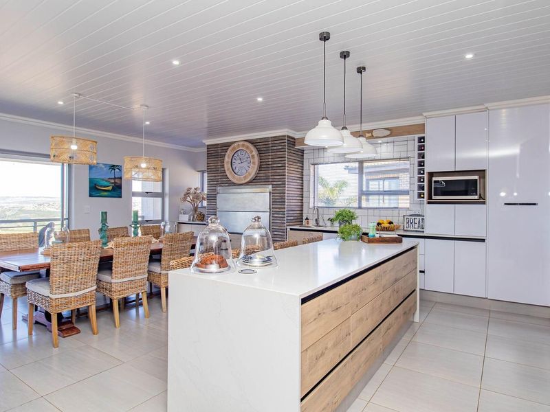 Modern open-plan kitchen and dining area featuring a large central island, sleek cabinetry, integrated appliances, and direct access to a patio with scenic views.